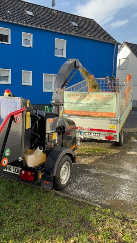 Ein Lkw mit einem Holzschnitzelgerät parkt vor einem blauen Gebäude.
