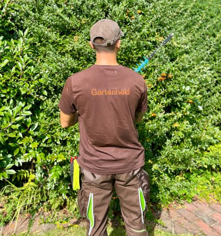 Mann mit Rückansicht schneidet eine Hecke mit einer elektrischen Heckenschere.